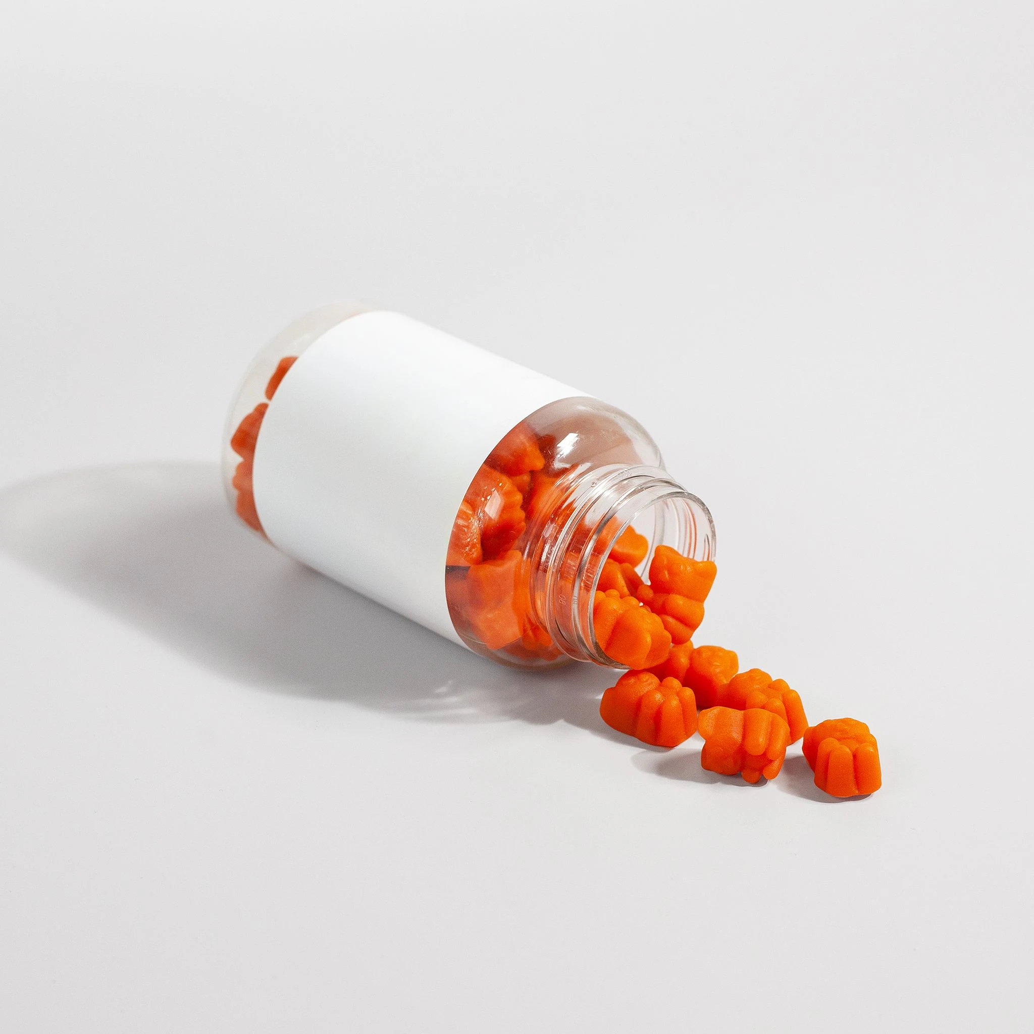 Orange gummy vitamins spilling from a clear bottle on a white surface