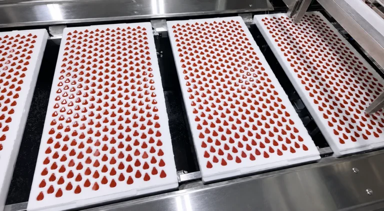 Red supplement gummies arranged in production trays
