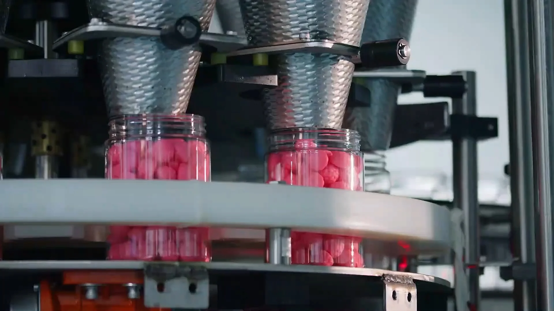 Clear jars of pink gummies beneath a bottling machine.