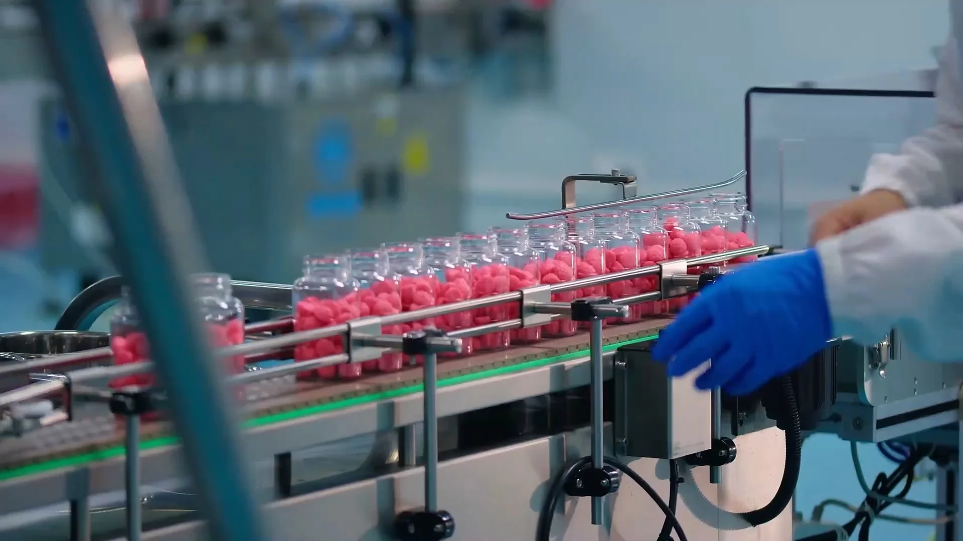Gloved worker inspecting gummies on a production line.