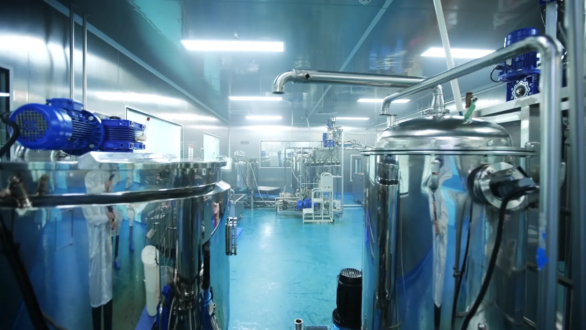 Stainless steel processing tanks with motors and connecting pipes in a production room.
